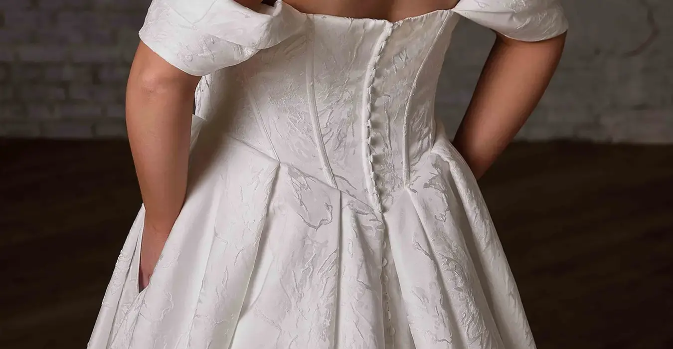 Close-up of the back of Eddy K ballgown wedding dress with a straight neckline and an off-shoulder body on a bridal model posing in a studio.