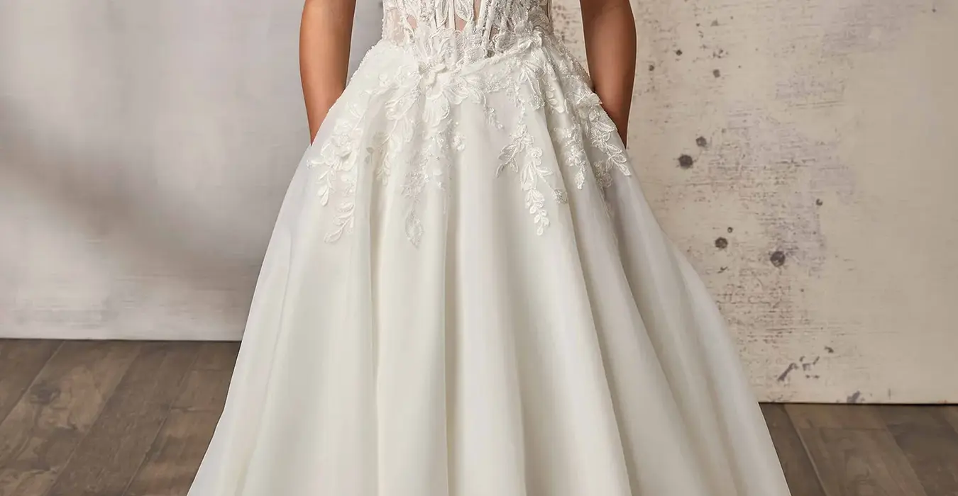Eddy K lace ballgown wedding dress with a scoop neckline and a sleeveless bodice on a bridal model standing in an elegant studio.
