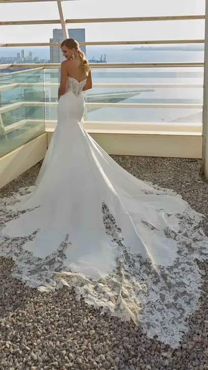 Back of Eddy K lace mermaid wedding dress with a sweetheart neck neckline and a trapless body on a bridal model standing on a rooftop of a skyscraper on a sunny day with a view of the city in the background