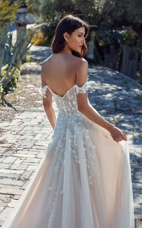Back close up of Eddy K lace and tulle ballgown with soft V back, 3D chiffon appliques and off-shoulder straps on bride walking in garden. 