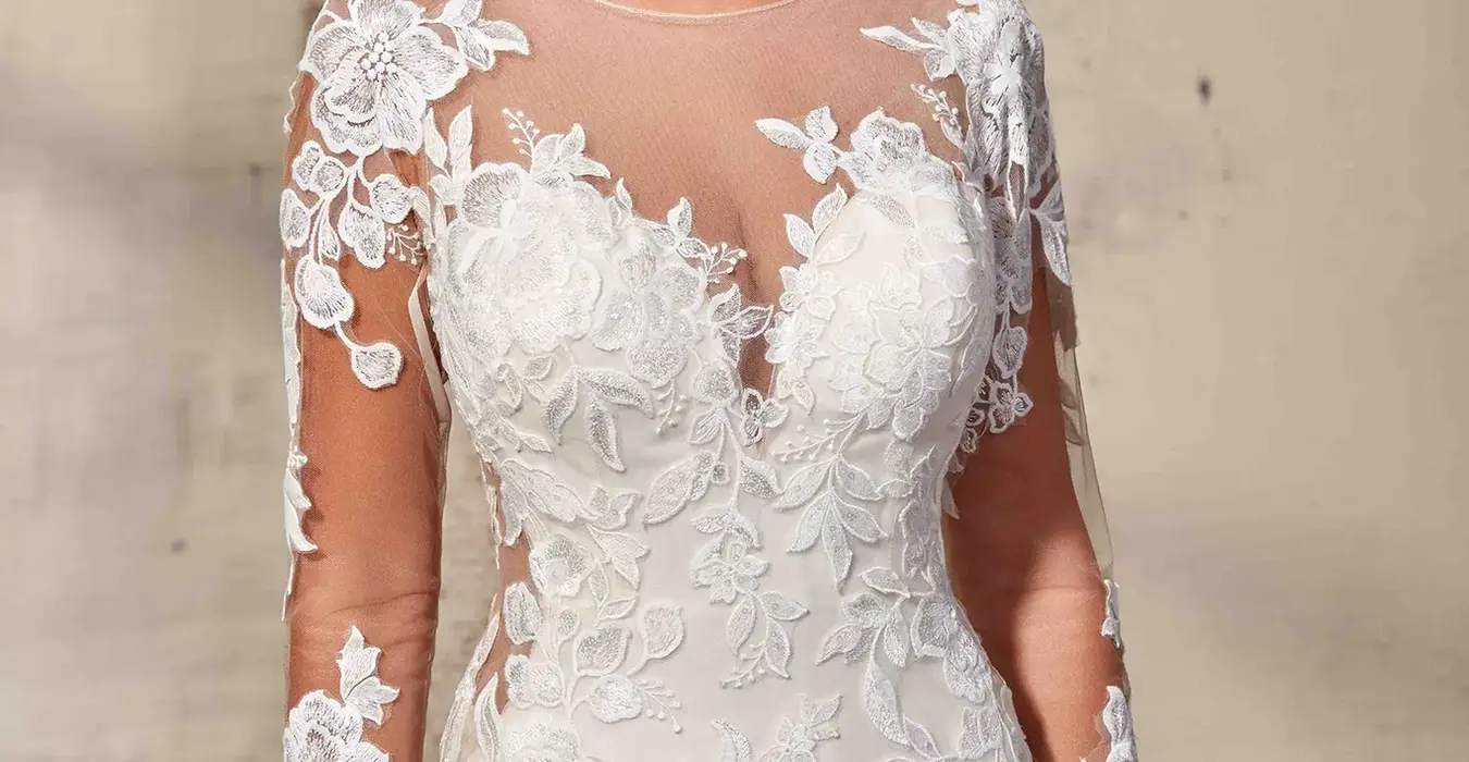 Close up of Eddy K lace wedding dress with illusion long sleeves on bridal model standing in studio.