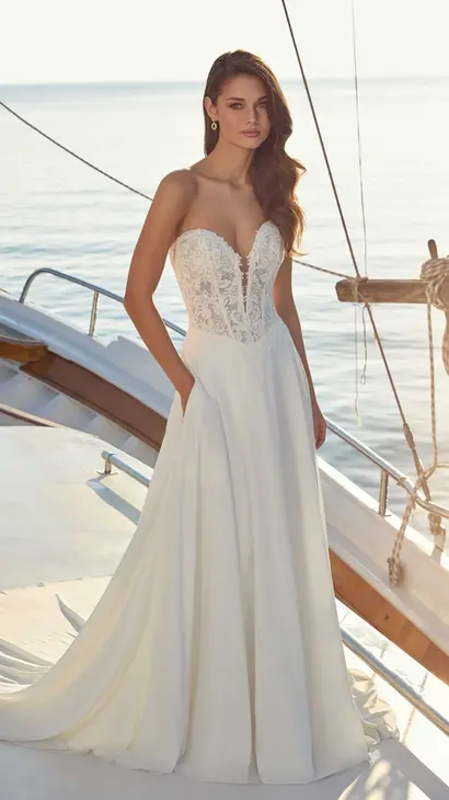 Eddy K crêpe a-line wedding dress with a sweetheart neckline and a strapless body on a bridal model standing on a yacht with the sea visible in the background.