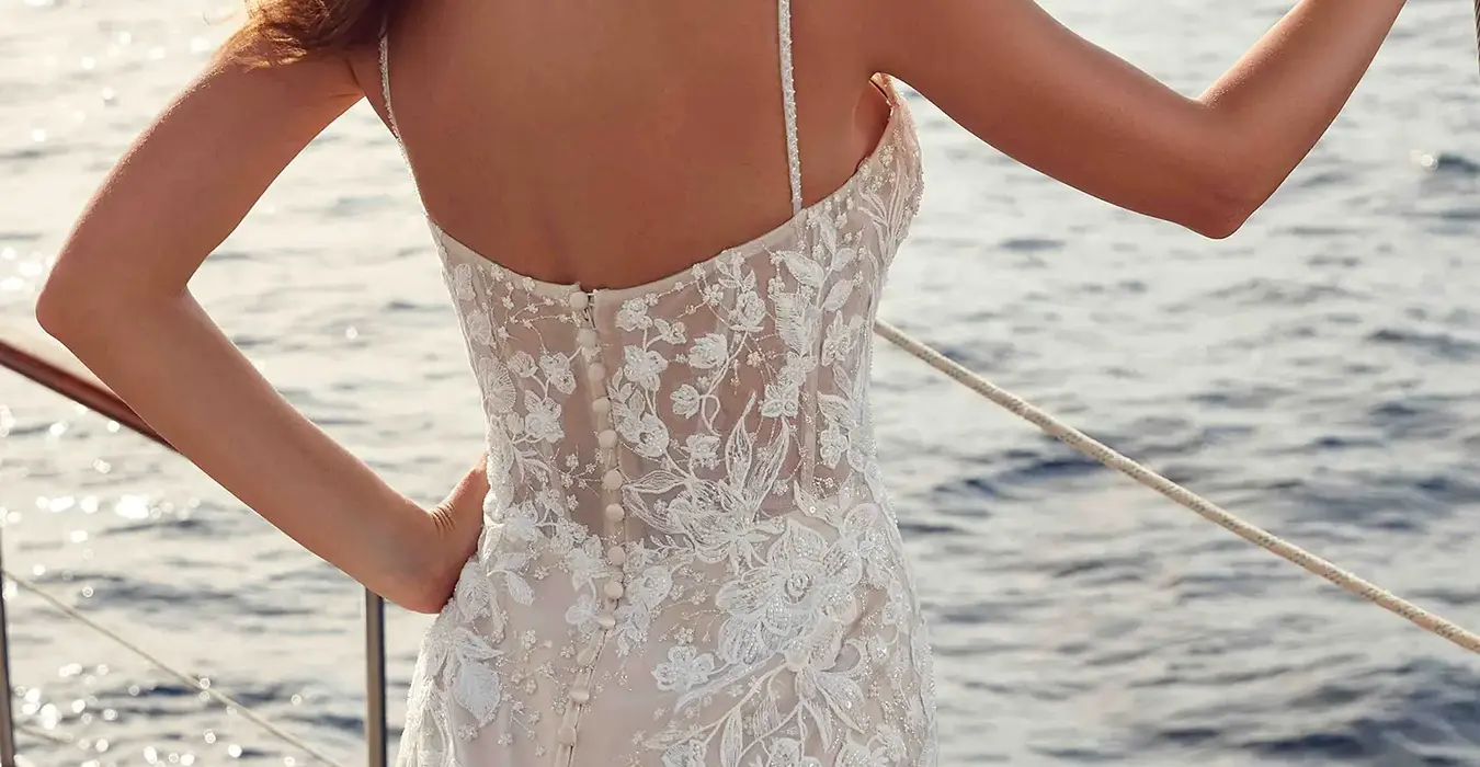 Back of a brunette woman wearing an Eddy K mermaid lace gown with spaghetti straps on a boat