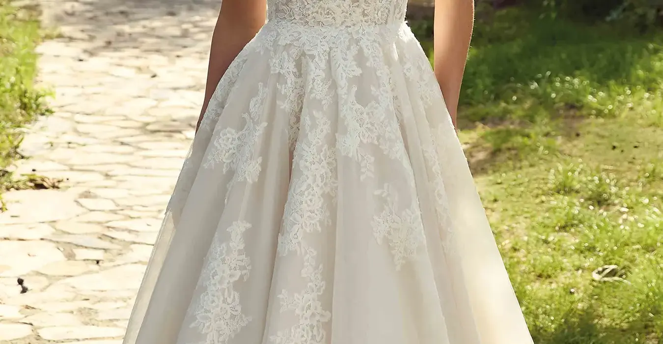 Eddy K tulle/lace ballgown wedding dress with a sweetheart neckline and a long sleeves body on a bridal model posing in a nice garden surrounded by threes.