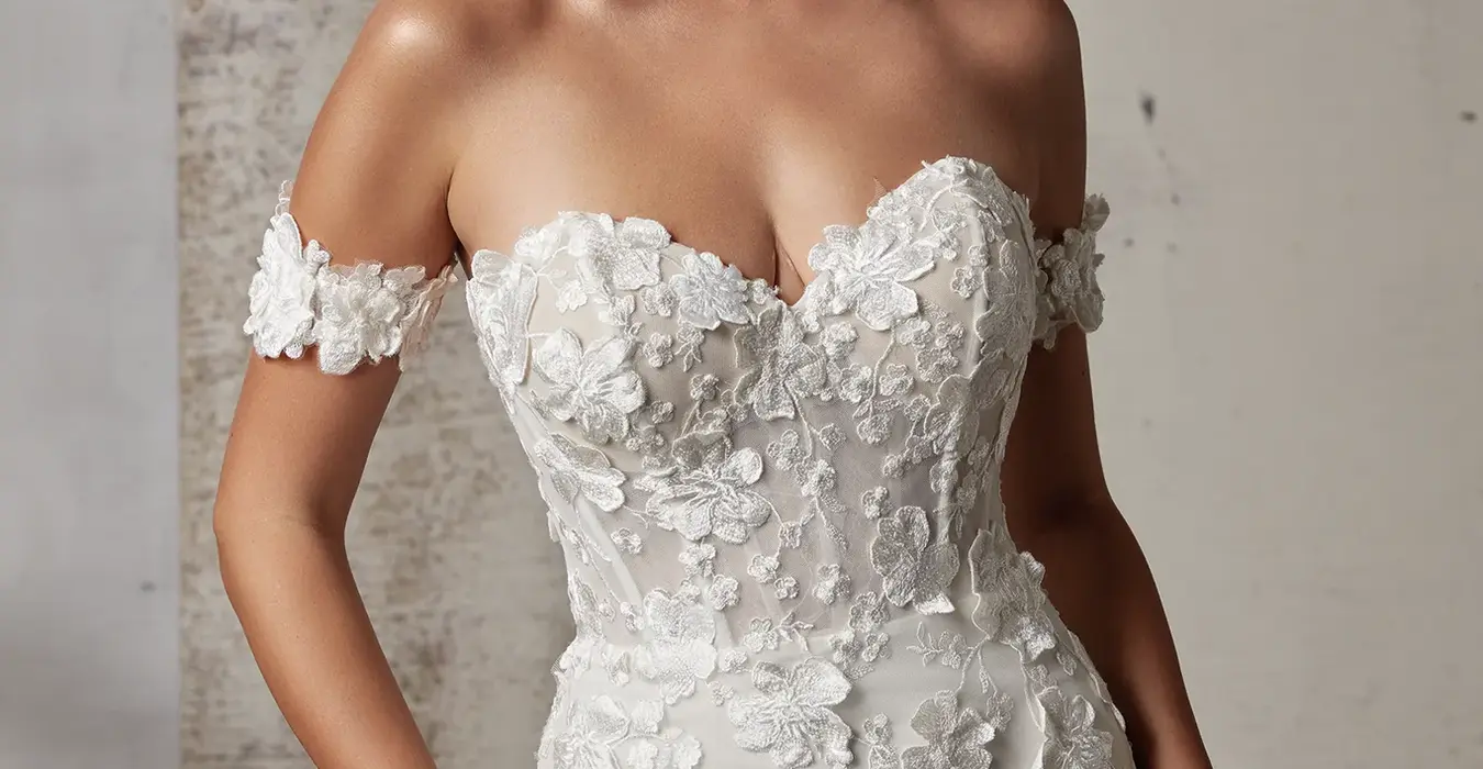 Close up of Eddy K fitted lace wedding gown with unlined Chantilly lace bodice with a sweetheart neckline and detachable lace armbands on bridal model posing in a studio.