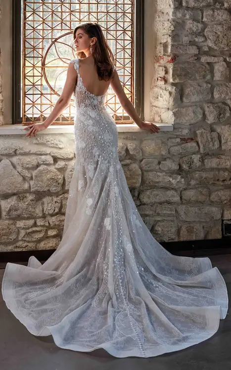 Back of Eddy K sleeveless fit-n-flare wedding dress with scoop back, 3D lace appliques and open train on bridal model in front of window