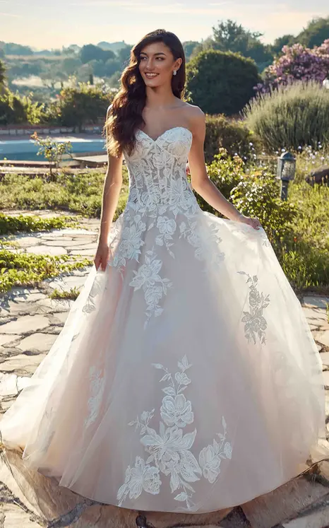 bride wearing wedding ballgown by wedding dress designer Eddy K with ivory lace and minimal beading over ivory tulle, lavender tulle & matte lining, unlined skin bodice, lavender buttons to end of train and drop waist. She is photograph in a beautiful garden.
