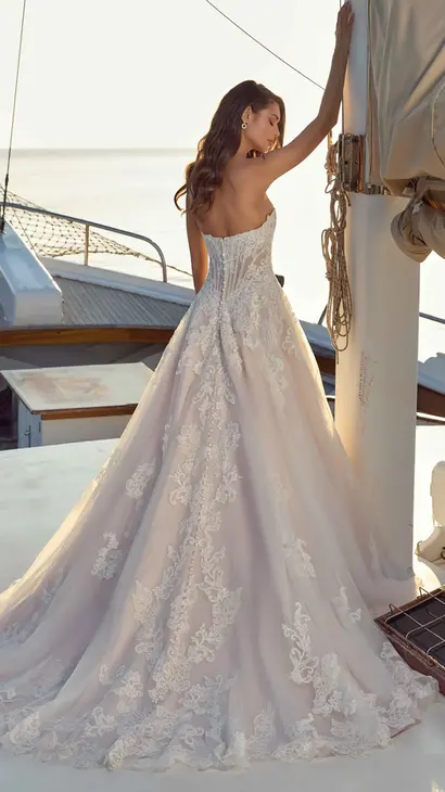 Back of Eddy K lace/tulle ballgown wedding dress with a straight neckline and a strapless body on a bridal model standing on a yacht on a sunny day.