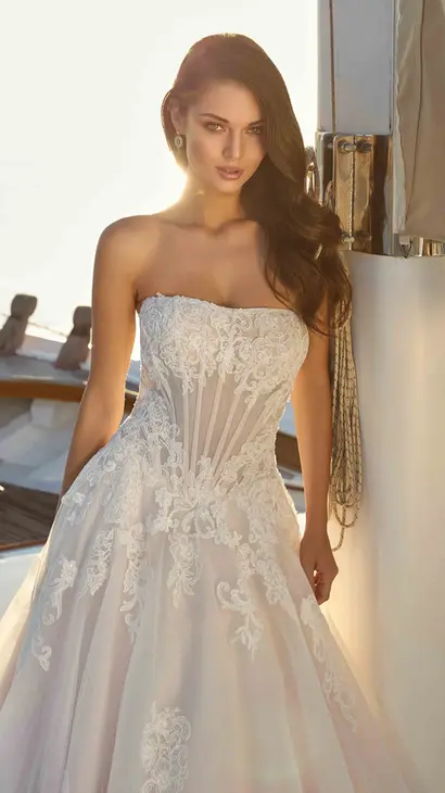Close up of Eddy K lace/tulle ballgown wedding dress with a straight neckline and a strapless body on a bridal model standing on a yacht on a sunny day.