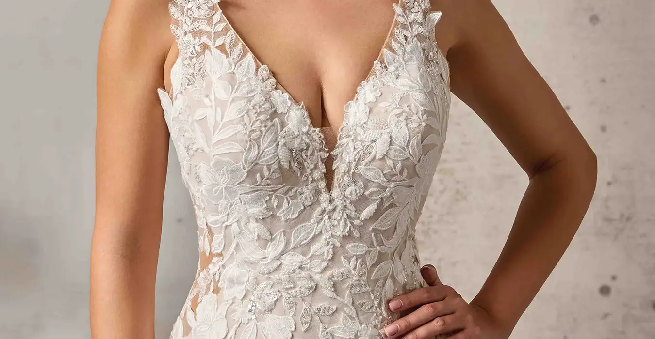 Close up of Eddy K lace and tulle fit-n-flare wedding dress with a v-neck neckline and a sleeveless body on a bridal model standing in a bridal studio.