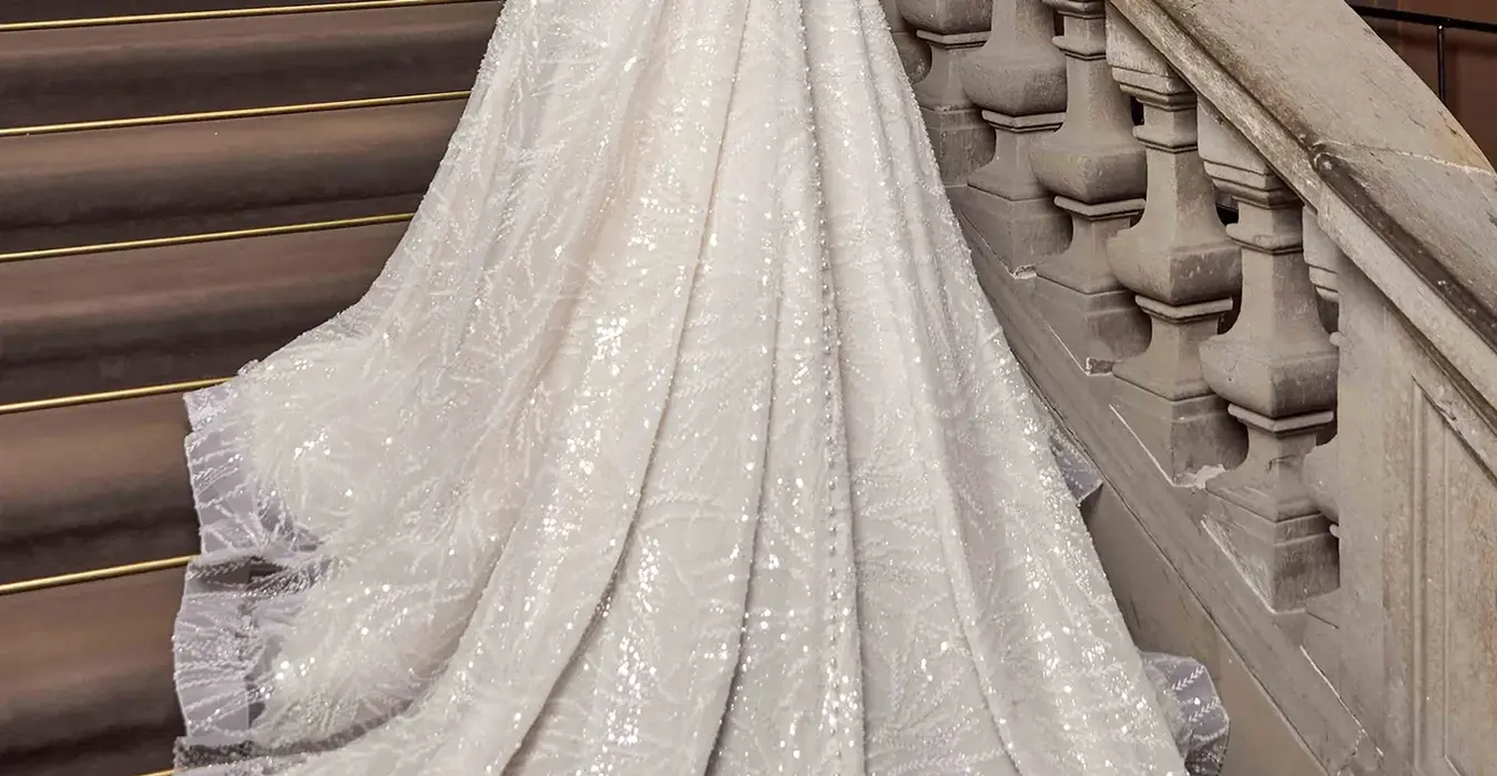 Back of Eddy K tulle a-line wedding dress with v-neck neckline  and dedicated beaded spaghetti straps on a bridal model standing on an elegant stair.
