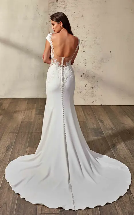 Back of Eddy K crepe and lace fit-n-flare with cap sleeves and illusion back on bridal model standing in a studio with open train.