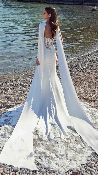 Back of Eddy K satin fit-n-flare wedding dress with a sweetheart neckline and a strapless body on a bridal model standing on rocky beach.