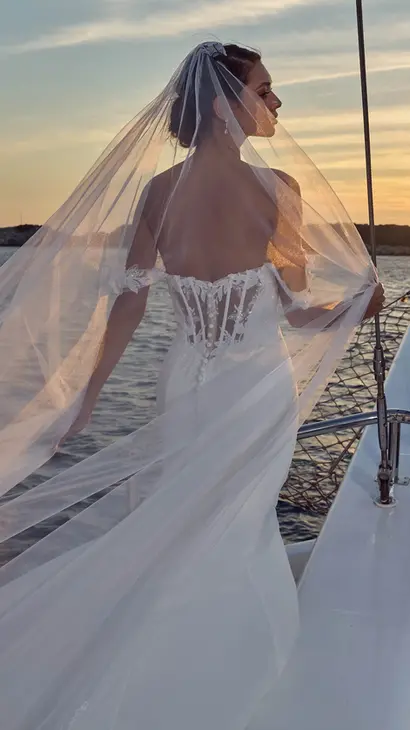 Close of back Eddy K crêpe fit-n-flare wedding dress with a sweetheart neckline and an off-shoulder body on a bridal model posing on a yacht in a beautiful afternoon.