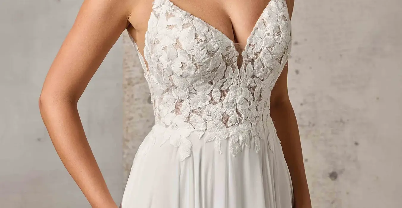 Close up of Eddy K chiffon a-line wedding dress with a v-neck neckline and a sleeveless body on a bridal model posing in a studio.