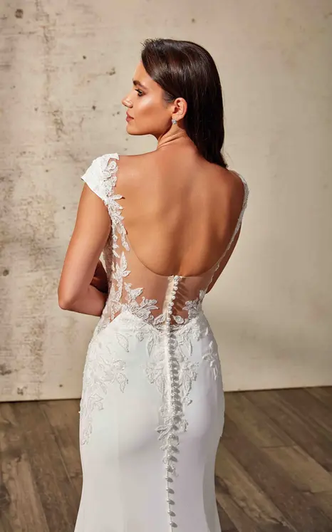Back of Eddy K fit-n-flare wedding dress with lace of crepe, cap sleeves and illusion back on bridal model standing in a studio.