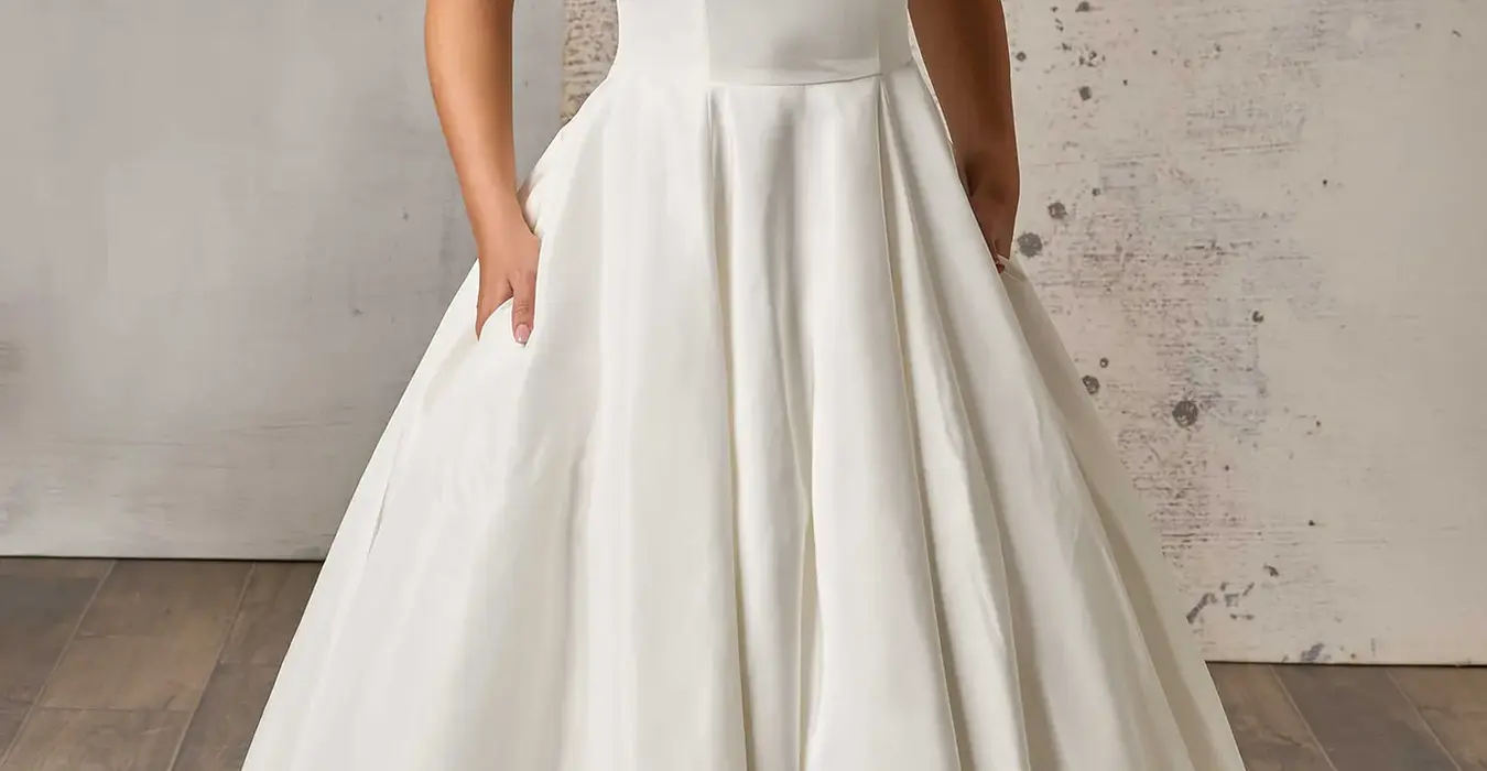 Eddy K taffeta ballgown wedding dress with a scoop neckline and a sleeveless body on a bridal model posing in a bridal studio.