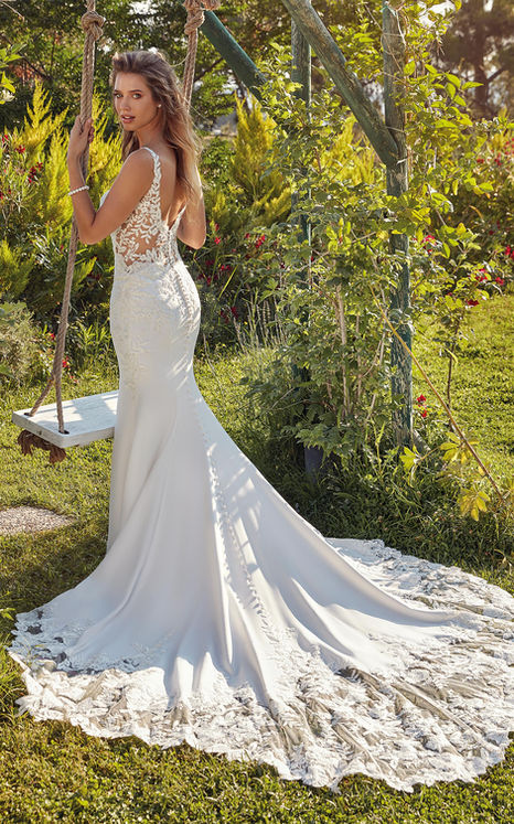 Back of Eddy K fit-n-flare wedding gown on woman with long blonde hair standing by tree swing set.