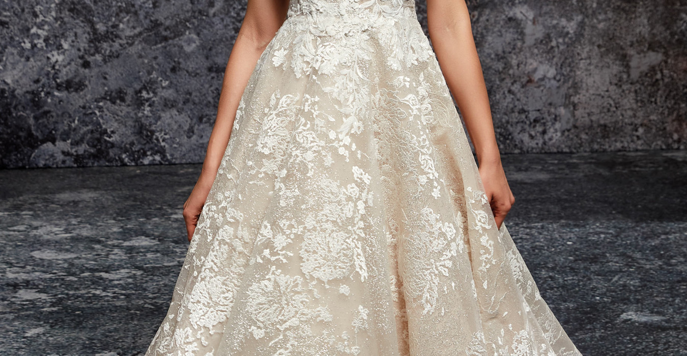 Woman wearing Eddy K ballgown wedding gown with ivory 3D lace and sequins over glitter tulle with spaghetti straps in studio