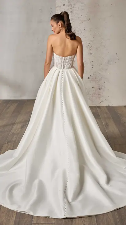 Back of Eddy K mikado fit-n-flare wedding dress with a sweetheart neckline and a strapless body on a bridal model standing in a bridal studio