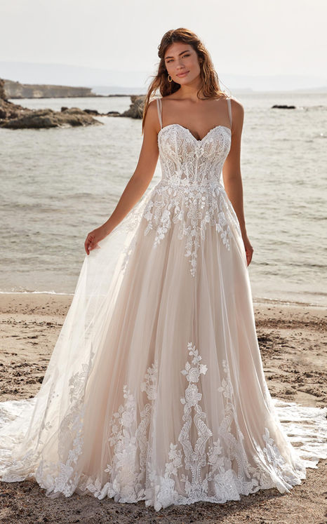 Eddy K wedding gown on brunette woman standing on beach by water. 