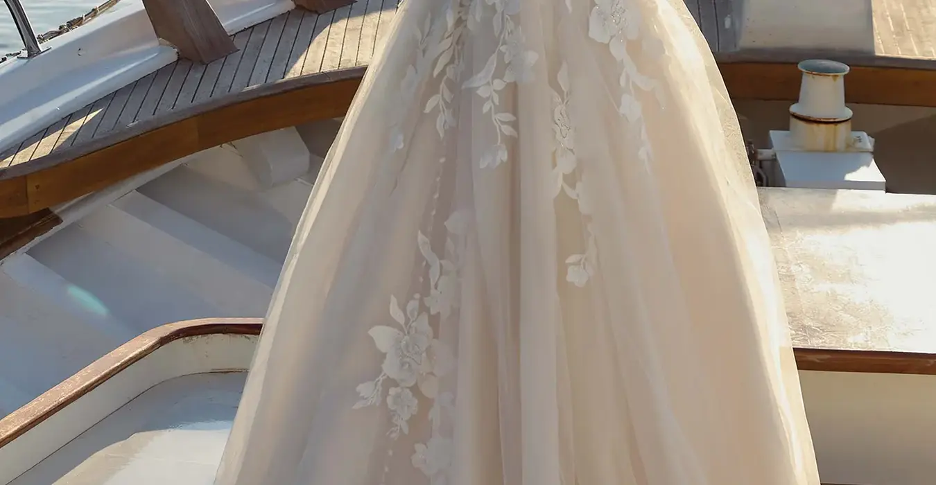 Back of Eddy K tulle ballgown wedding dress with a straight neckline and a strapless body on a bridal model posing on a yacht on a sunny day near the coast