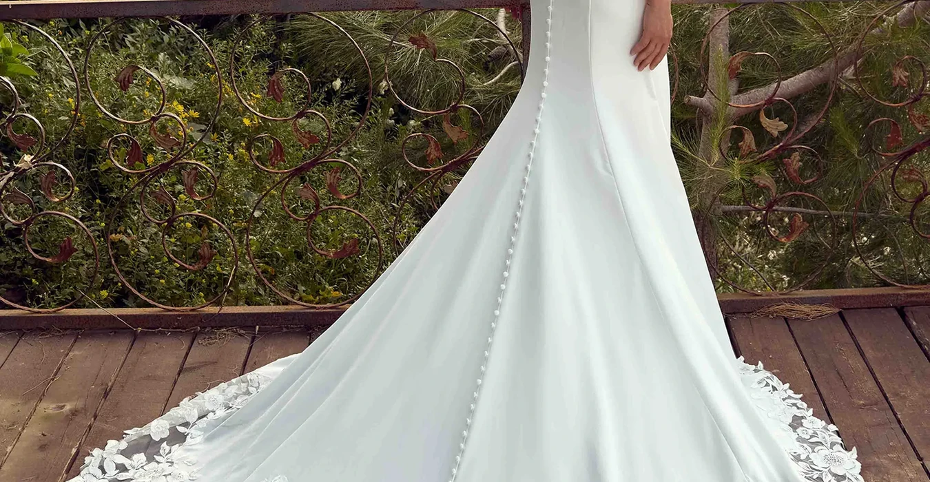 Back of Eddy K crepe fit-n-flare wedding dress with a sweetheart neckline and a sleeveless bodice on a bridal model standing in an elegant garden