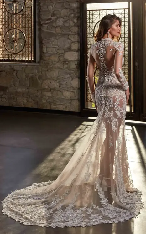 Back of Eddy K long sleeve fit-n-flare wedding dress with unlined bodice and skirt and beaded lace over tulle on bride standing in the light of the window