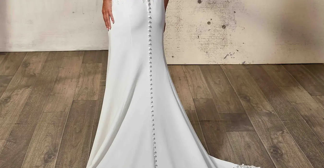 Back of Eddy K fit-n-flare  sleeveless crepe and lace wedding gown with open train with scalloped edges on bridal model photographed in a studio.