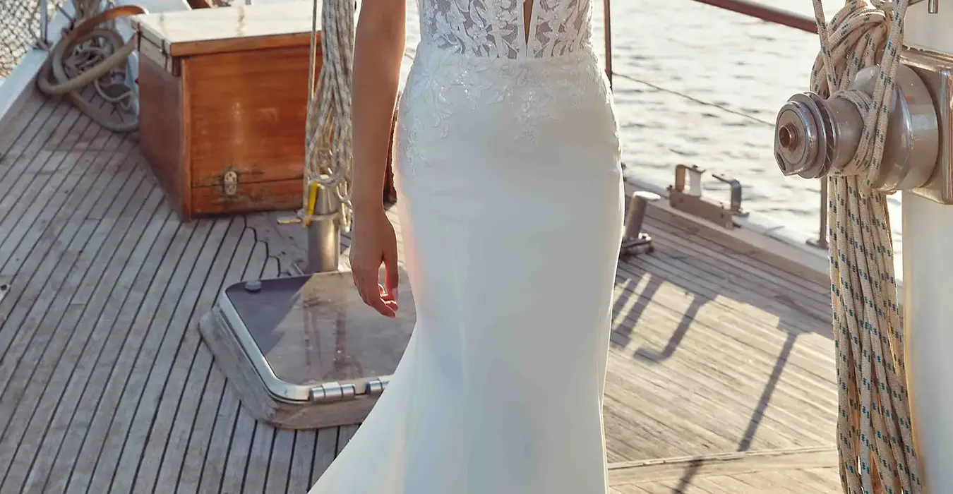 Eddy K fit-n-flare wedding gown with lace corset bodice with spaghetti straps over crepe skirt on bride standing on a boat at sunset.