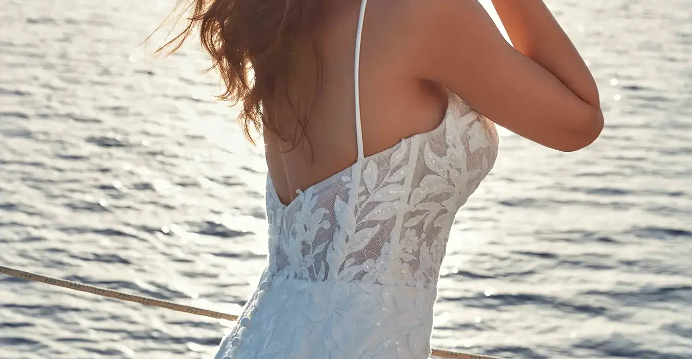 Back close up of Eddy K wedding gown with lace corset bodice and spaghetti straps and crepe skirt on bride on a boat at sunset.