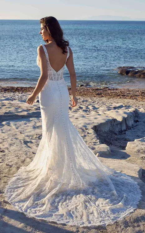 Back of Eddy K lace fit-n-flare wedding dress with a v-neck neckline and a sleeveless bodice on a bridal model standing on a sunny beach