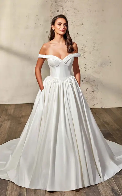 bride wearing mikado ballgown by wedding dress designer Eddy K Mikado with off shoulder sleeves, corset basque waist bodice, buttons to end of train, pockets. She is photographed in a beautiful studio.