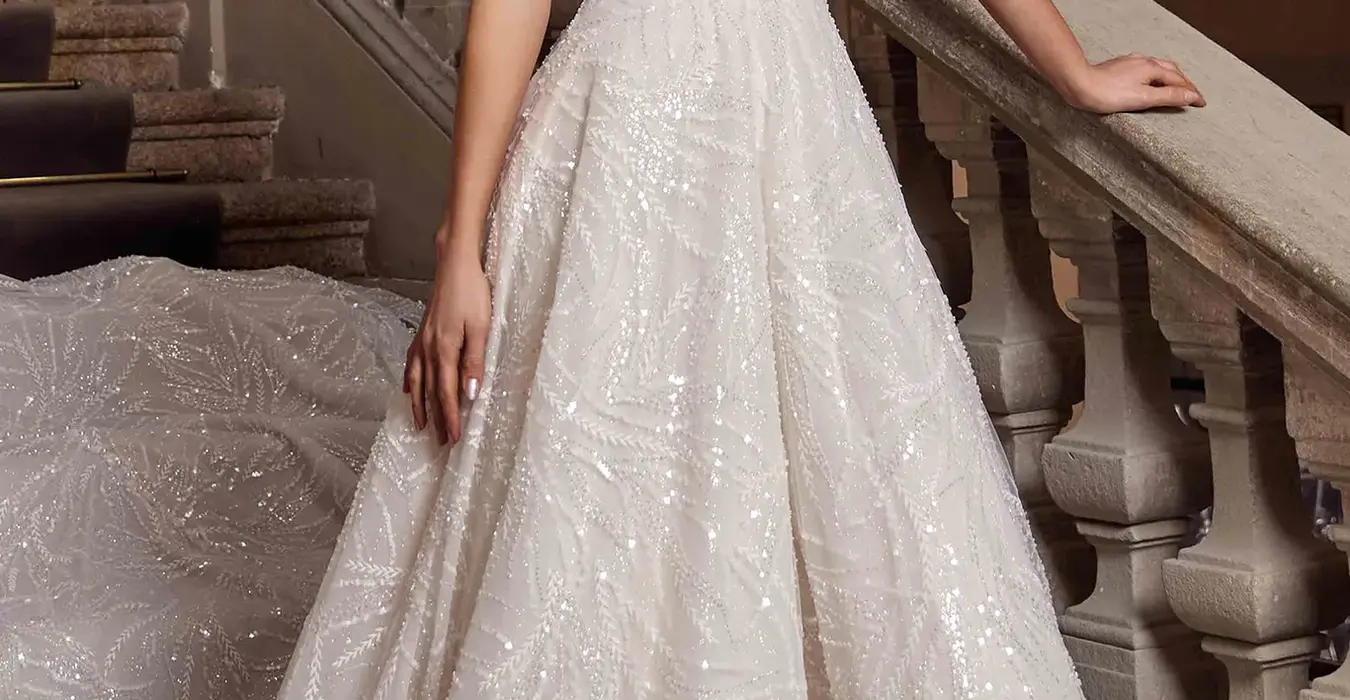 Eddy K tulle a-line wedding dress with v-neck neckline  and dedicated beaded spaghetti straps on a bridal model standing on an elegant stair.