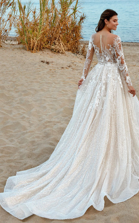 Back of Eddy k wedding gown with long sleeeves and glitter tulle on brunette woman on beach.