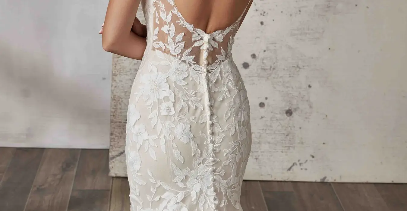 Close back of Eddy K lace wedding dress with shimmer tulle, open back and spaghetti straps on bridal model with hair in a ponytail standing in a studio.
