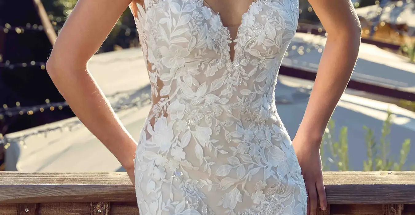Close up of Eddy K lace and tulle fit-n-flare wedding dress with a v-neck neckline and a sleeveless body on a bridal model standing on a terrace with a nice scenery on the background.