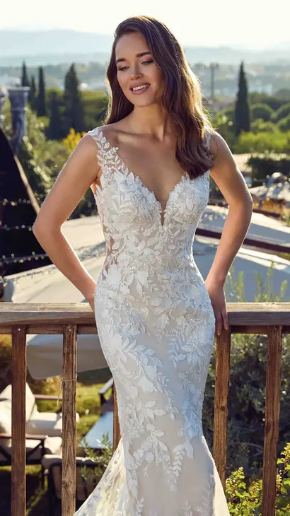 Close up of Eddy K lace and tulle fit-n-flare wedding dress with a v-neck neckline and a sleeveless body on a bridal model standing on a terrace with a nice scenery on the background.