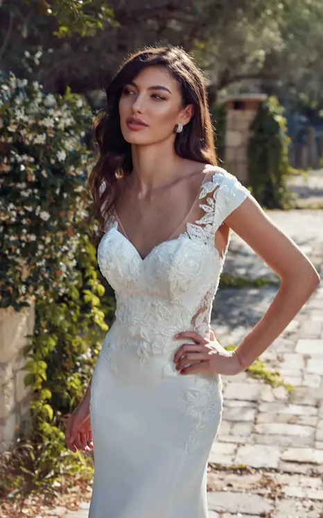 Close up of Eddy K fit-n-flare gown with ivory lace over crepe and cap sleeves on bride posing in rustic garden.