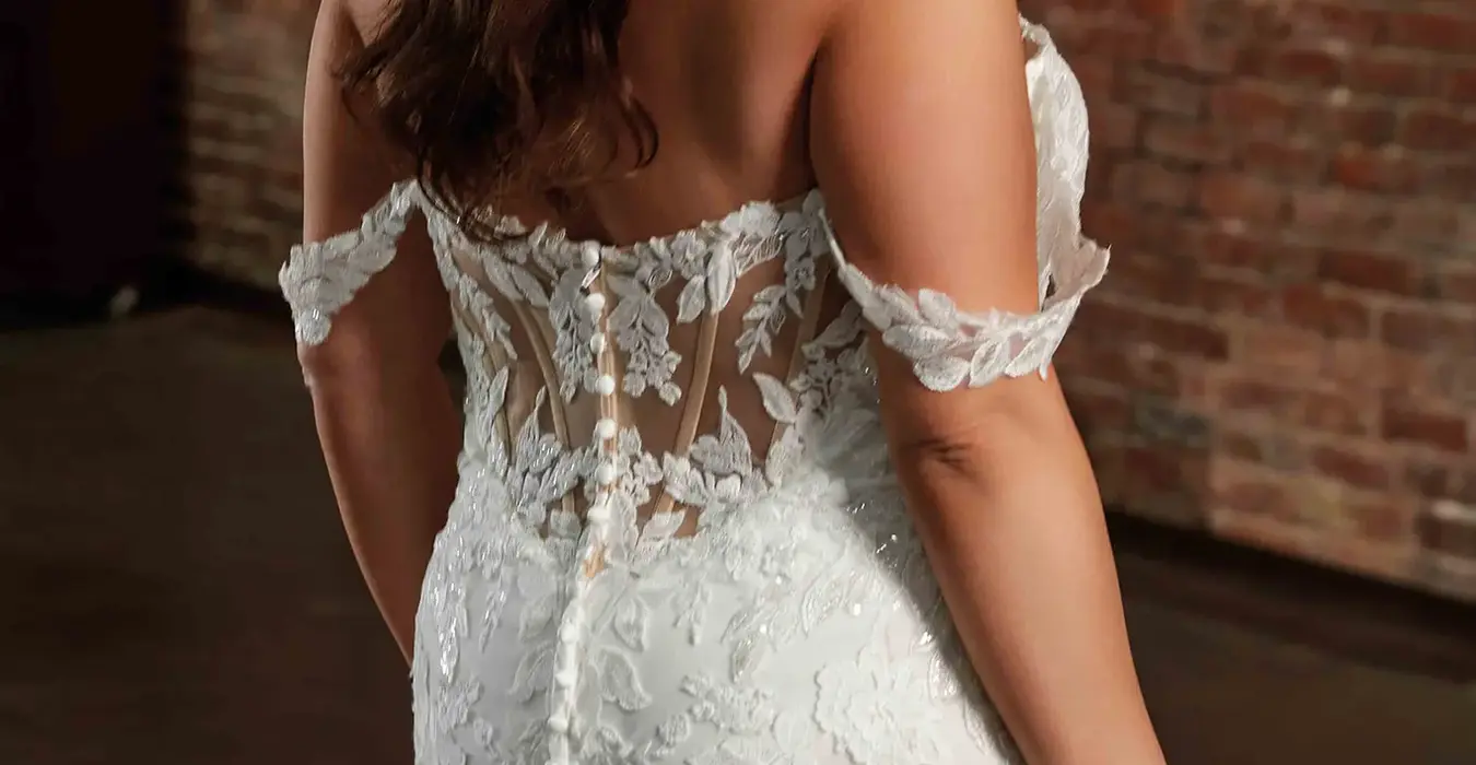 Back close up of Eddy K lace wedding dress with unlined back on bridal model looking to the side in warehouse setting