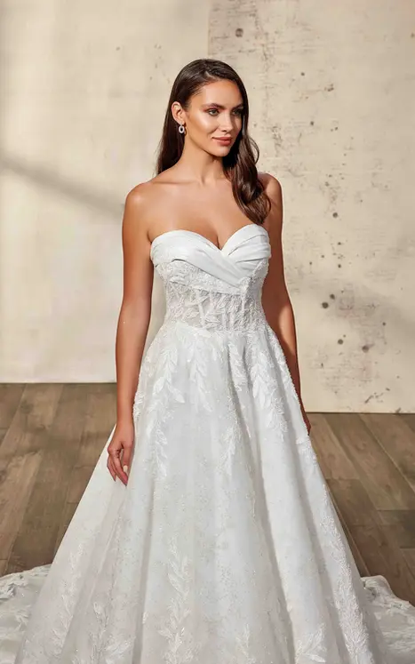 close up bride wearing ballgown by wedding dress designer Eddy K with beaded ivory lace and sequins, sequin embroidered glitter tulle, champagne tulle, champagne pleated satin trim around neckline, champagne matte lining, skin unlined bodice, buttons to end of train, lace up over zipper back. She is photographed in beautiful minimalist studio