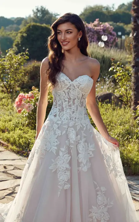 close up is bride wearing wedding ballgown by wedding dress designer Eddy K with ivory lace and minimal beading over ivory tulle, lavender tulle & matte lining, unlined skin bodice, lavender buttons to end of train and drop waist. She is photograph in a beautiful garden.