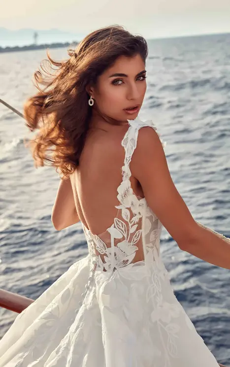 Back close up of Eddy K organza and lace wedding dress with unlined back and lace straps on bride on a boat facing the ocean.