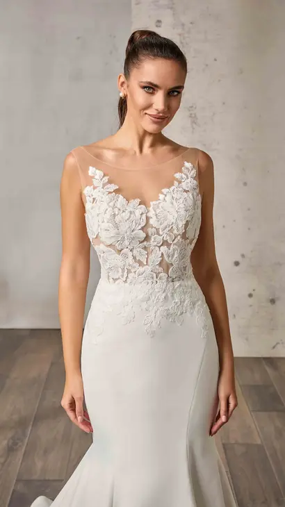 Close up of Eddy K satin mermaid wedding dress with an illusion neckline and a sleeveless body on a bridal model standing in bridal studio.