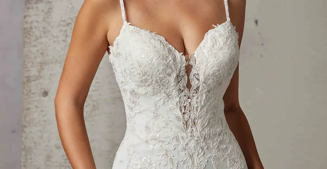 Close up of Eddy K crepe wedding dress with spaghetti straps and skin cleavage with lace on bodice on bridal model posing in studio.