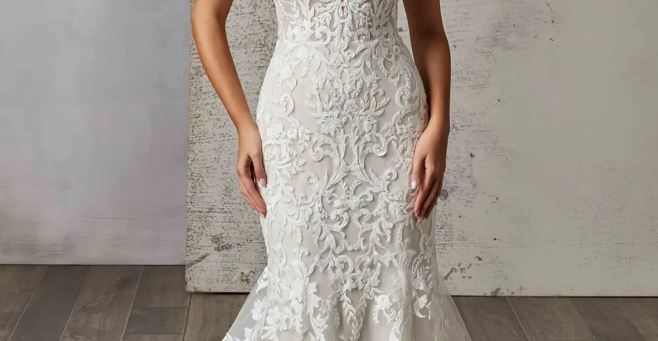Eddy K fit-n-flare all over lace wedding dress with lace straps and skin cleavage on bridal model standing in studio.