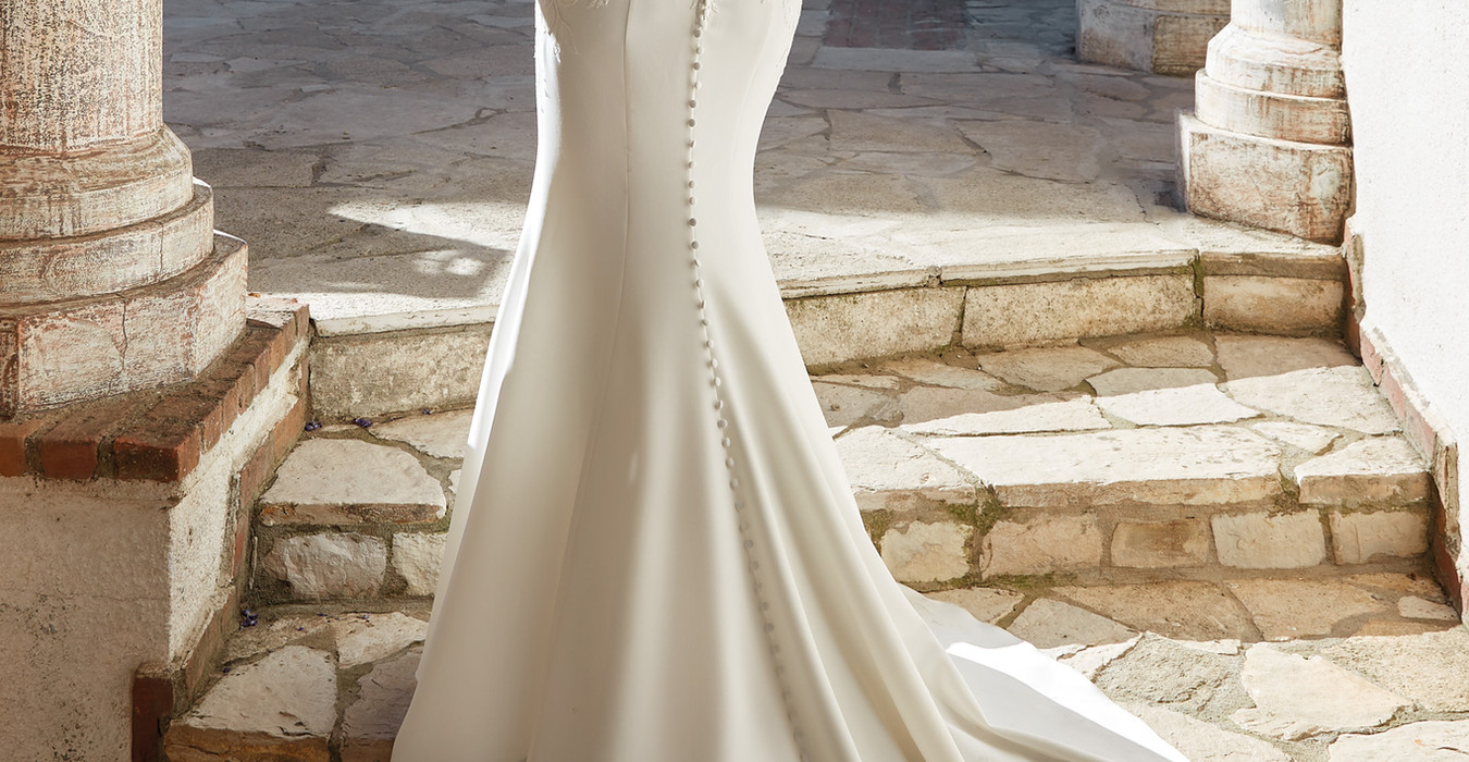 Back of Eddy K Crepe mermaid wedding gown on blonde model with pony tail.