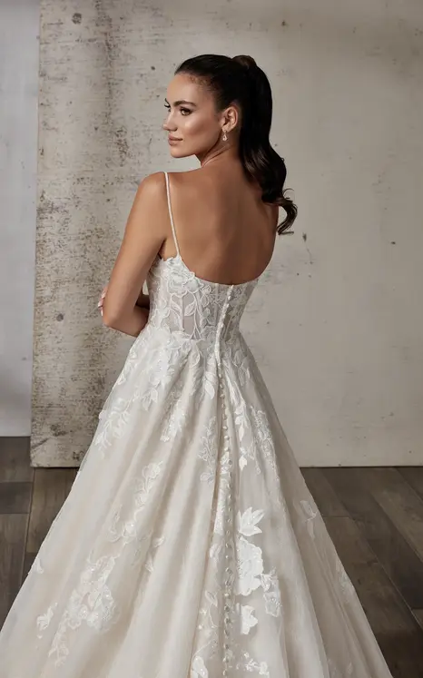 Back close up of Eddy K wedding dress in lace and tulle with spaghetti straps and scoop back on bridal model standing in studio with hair in a ponytail.