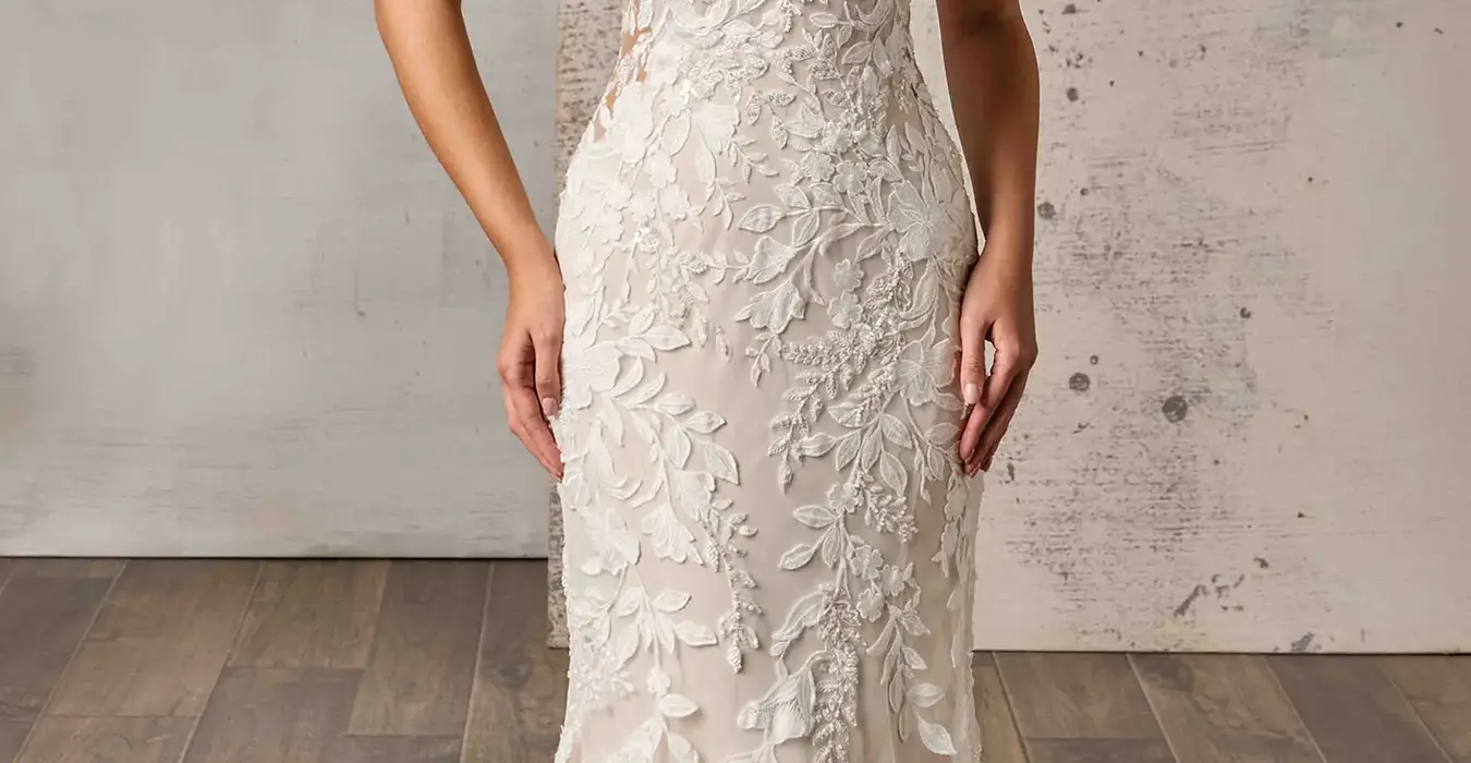 Eddy K lace and tulle fit-n-flare wedding dress with a v-neck neckline and a sleeveless body on a bridal model standing in a bridal studio.