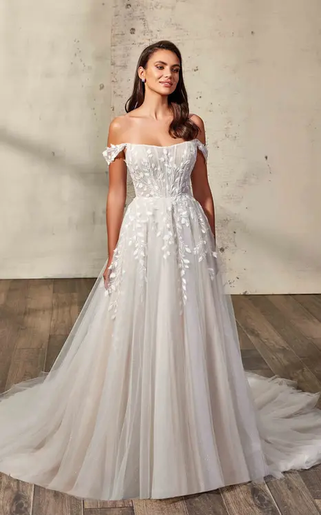 Eddy K lace and tulle ballgown with chiffon appliques and off-shoulder straps on a bridal model standing in studio with her hair down.